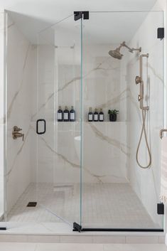 a walk in shower sitting next to a white tiled wall and floor with glass doors