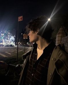 a young man standing on the side of a road at night with his hand out