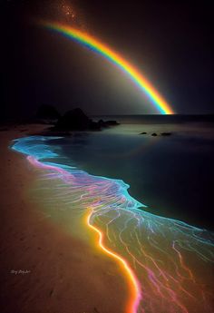 a rainbow in the sky over a beach with waves and water on it's side