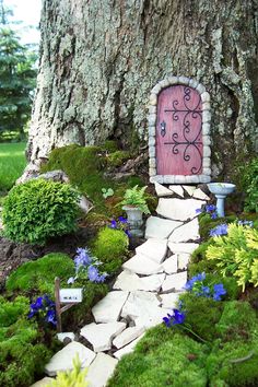 a fairy garden with a pink door in the middle of it and blue flowers on the ground