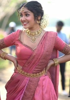 a woman in a pink sari with gold jewelry on her neck and hands behind her back