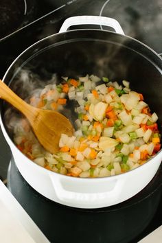 vegetables being cooked in a pot with a wooden spoon on the stove top next to an oven