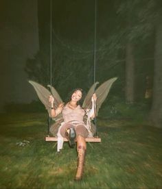 a woman sitting on a swing in the grass with her legs crossed and wings outstretched