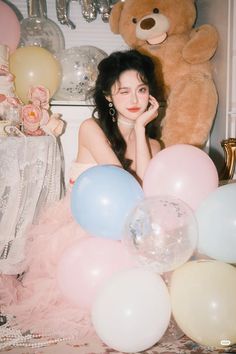 a woman sitting in front of balloons and a teddy bear with her hand on her face