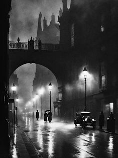 a black and white photo of people walking in the rain under an overpass at night