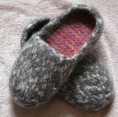 a pair of gray and pink slippers sitting on top of a bed