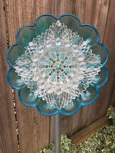 a blue and white glass flower on top of a metal pole in front of a wooden fence