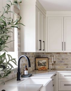 a kitchen with white cabinets and black faucet, marble counter tops and an olive tree in the corner