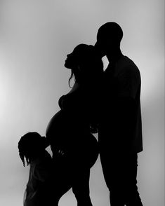 a man and woman standing next to each other with their arms around the pregnant child