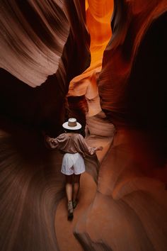 the woman is walking through the narrow slots in the canyon, wearing a hat and white shorts