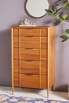 a tall wooden dresser sitting next to a mirror on top of a purple painted wall