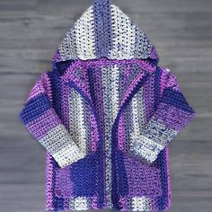 a purple and white crocheted jacket hanging on a hook in front of a wooden wall