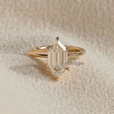 a gold ring with an emerald cut diamond on top, sitting on a white blanket