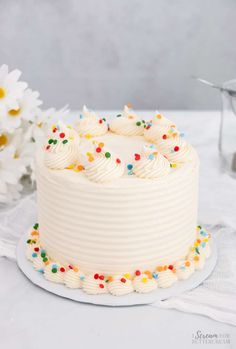 a cake with white frosting and sprinkles on a plate next to flowers