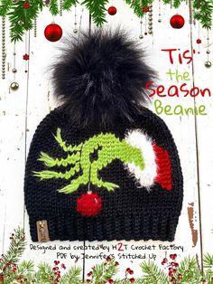 a knitted hat with a green and red dragon on it, sitting in front of christmas decorations