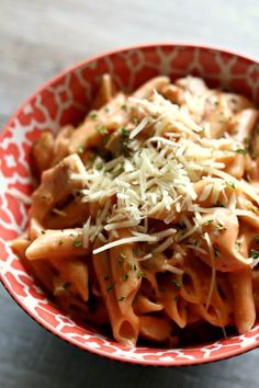 a red and white bowl filled with pasta covered in parmesan cheese