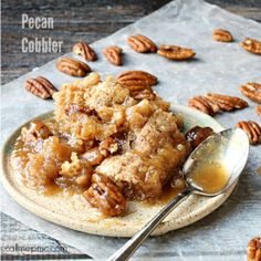 pecan cobbler on a plate with a spoon and some pecans in the background