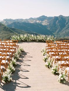 an outdoor ceremony set up with wooden chairs and greenery on the aisle, overlooking mountains