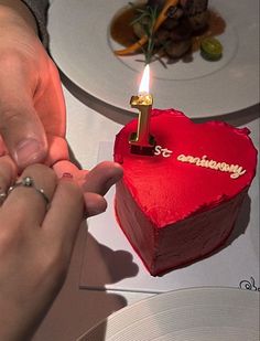 a person lighting a candle on top of a heart shaped cake