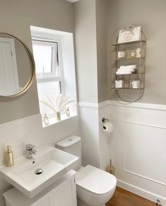 a white toilet sitting next to a sink in a bathroom under a mirror above a window