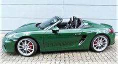 a green sports car parked in front of a garage door with the top down on it's wheels