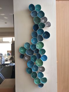 a wall sculpture made out of bowls hanging on the side of a white wall in a kitchen