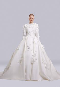 a woman in a white wedding dress with flowers on the skirt and long sleeved sleeves