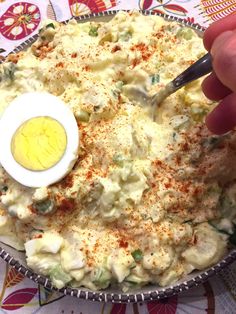 a person dipping an egg into a bowl of mashed potatoes with seasoning on the side