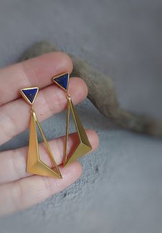 This elegant and modern earring is a new part of the Moment Collection and it has a geometric design. These sterling  silver earrings are handmade and unique. This pyramidal earring consists two parts. İn the upper part I used sterling silver (925) and 3D triangle lapis lazuli gemstone  with silver smithing technique. I made gold plated on silver (925 K). I used wax model technique in the lower part and I made gold plated. These earrings which have a diferent and contemporary design are suitable for daily and night use. You can choose it as a gift alternative for geometric jewelry lovers. Dimensions of lapis lazuli gemstone in the upper part are 0.9 cm* 0.9 cm. Dimensions of the lower part 4 cm * 1.5 cm. Total length of the earring is 5 cm. This item is ready to ship. All items are sent wi Geometric Brass Earrings For Gift, Modern Blue Brass Earrings, Handmade Modern Geometric Earrings, Modern Handmade Geometric Earrings, Triangle Metal Earrings For Gift, Modern Geometric Earrings For Pierced Ears, Contemporary Linear Earrings For Gifts, Modern Geometric Pierced Earrings, Modern Geometric Linear Earrings For Gifts