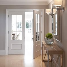 an entry way with two mirrors and a vase filled with flowers on top of a table