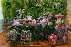 a table covered in lots of flowers and fairy figurines next to a green wall