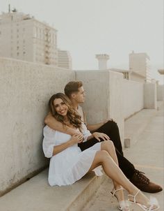 a man and woman sitting next to each other on the side of a cement wall