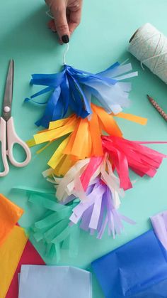 someone cutting up tissue paper with scissors on a blue table next to some crafting supplies