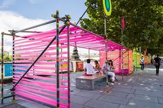 people are sitting on benches in front of colorfully painted structures and trees near the water