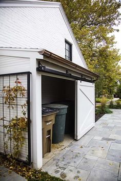 a white shed with a trash can in the door and some leaves on the ground