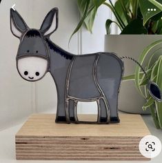 a small metal donkey sitting on top of a wooden block next to a potted plant