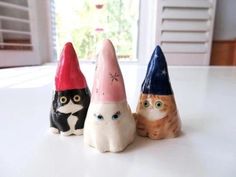 three small ceramic cats wearing hats on top of a white table next to a window