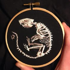 a person holding up a black and white embroidery with a skeleton on it's back