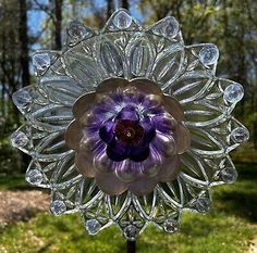 a purple flower made out of glass sitting on top of a wooden stand in the grass