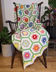 a chair with a quilt on it and a potted plant in the back ground