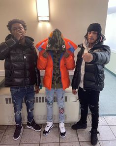 three young men standing next to each other in front of a heater with an orange and blue jacket on