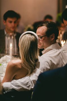 a man and woman sitting next to each other at a table with candles in the background