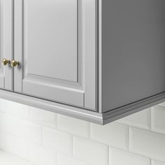 a close up of a kitchen cabinet with white tile on the wall and gold handles