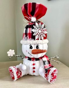 a snowman sitting on top of a table wearing a red and white hat, scarf and mittens