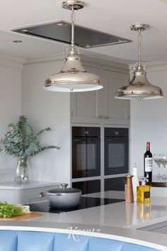 two lights hanging over a kitchen island with wine bottles and glasses on the counter top