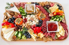 a platter filled with meats, cheeses and fruit on a wooden tray