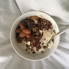 a bowl filled with granola and nuts on top of a white sheet covered bed