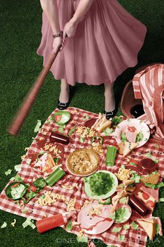 a woman holding a baseball bat standing next to a picnic blanket with food on it