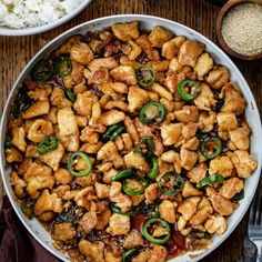 a pan filled with chicken and vegetables next to rice on top of a wooden table