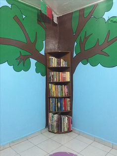 a room with a tree painted on the wall next to a book shelf filled with books